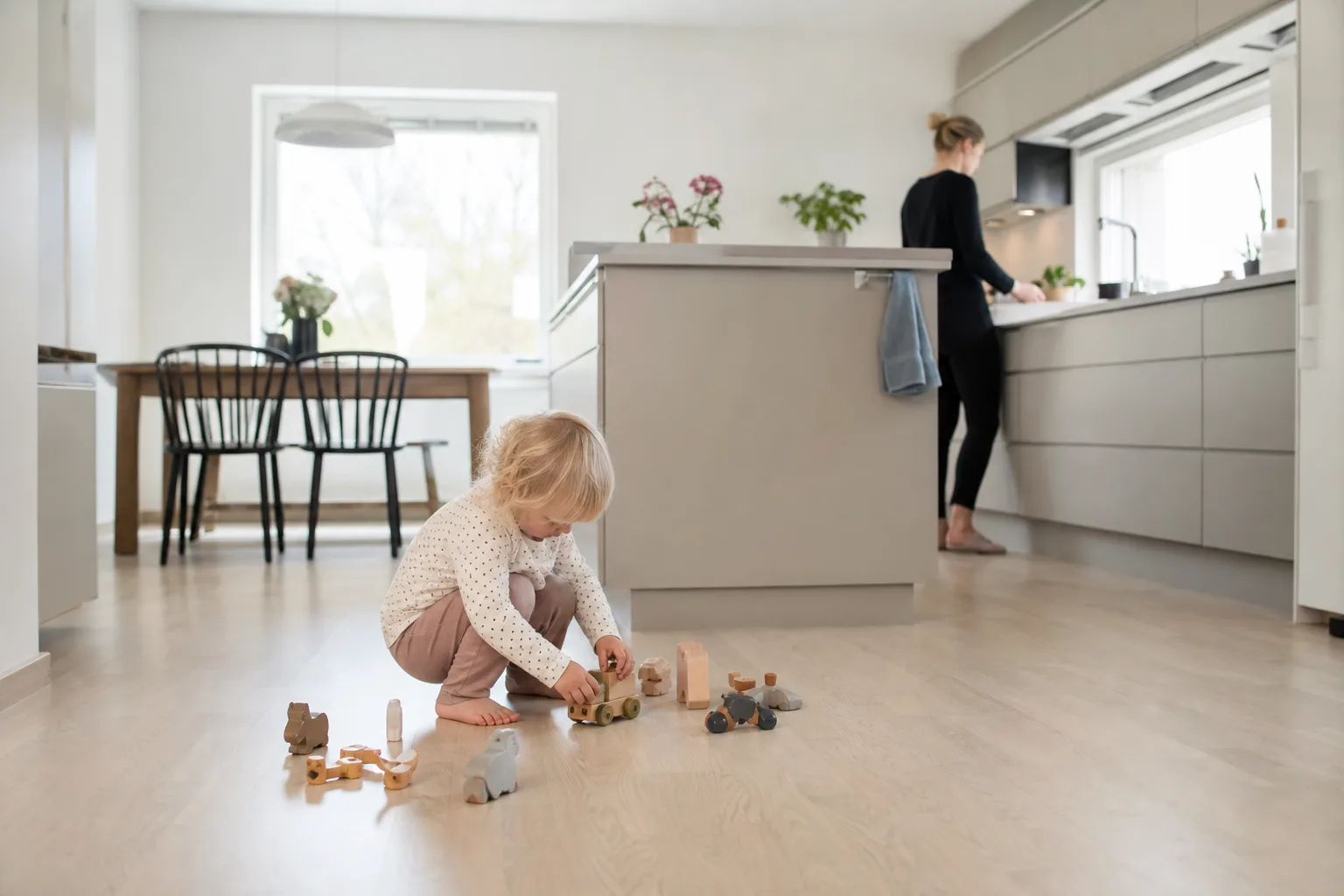 Barnfamilj i ett nystädat kök med lekande barn på golvet en vardagsmorgon